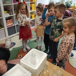 Dziewczynka stojąca z innymi przedszkolakami trzyma szklankę z suchym lodem