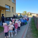 Przedszkolaki ustawione w parach stoją na chodniku przed przedszkolem
