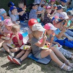 Dzieci siedzą na kocyku i konsumują owoce